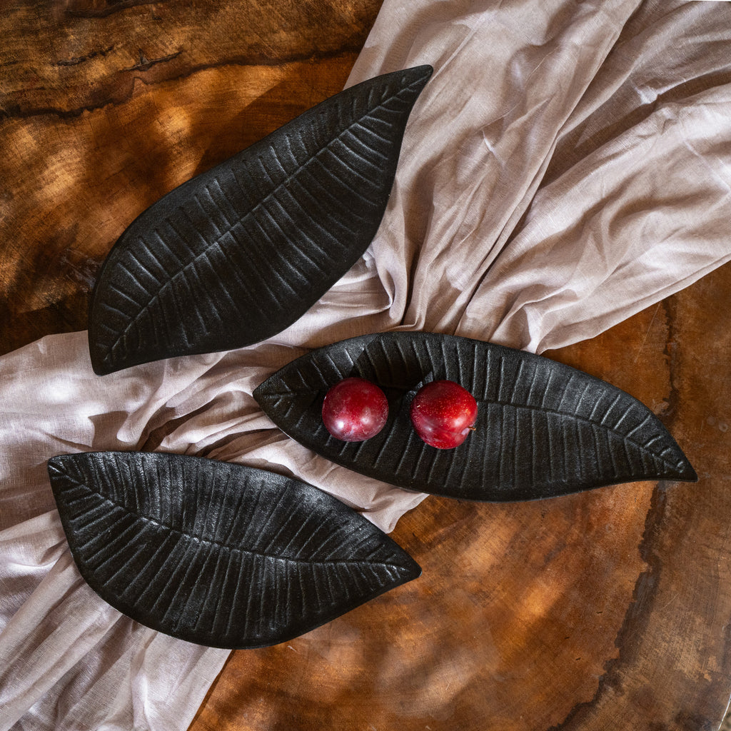 Set of three black wooden leaf-shaped serving platters with carved vein details