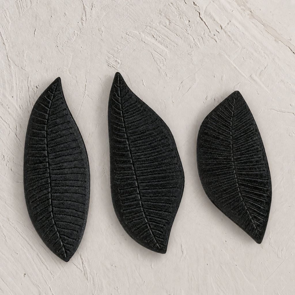 Set of three black wooden leaf-shaped serving platters with carved vein details