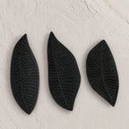 Set of three black wooden leaf-shaped serving platters with carved vein details