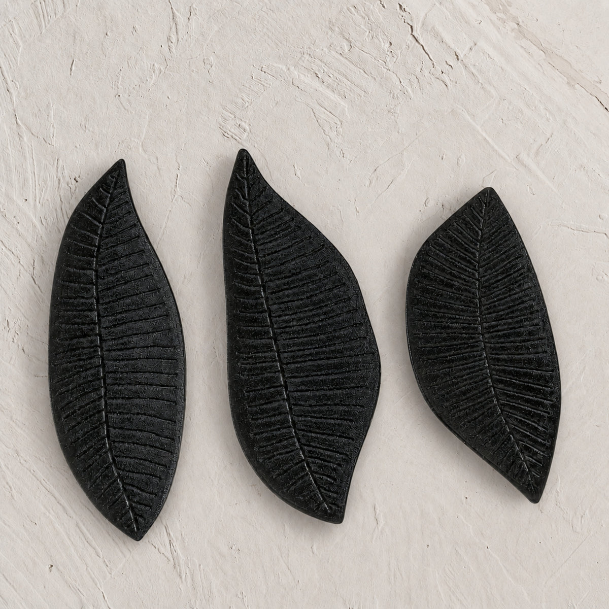 Set of three black wooden leaf-shaped serving platters with carved vein details