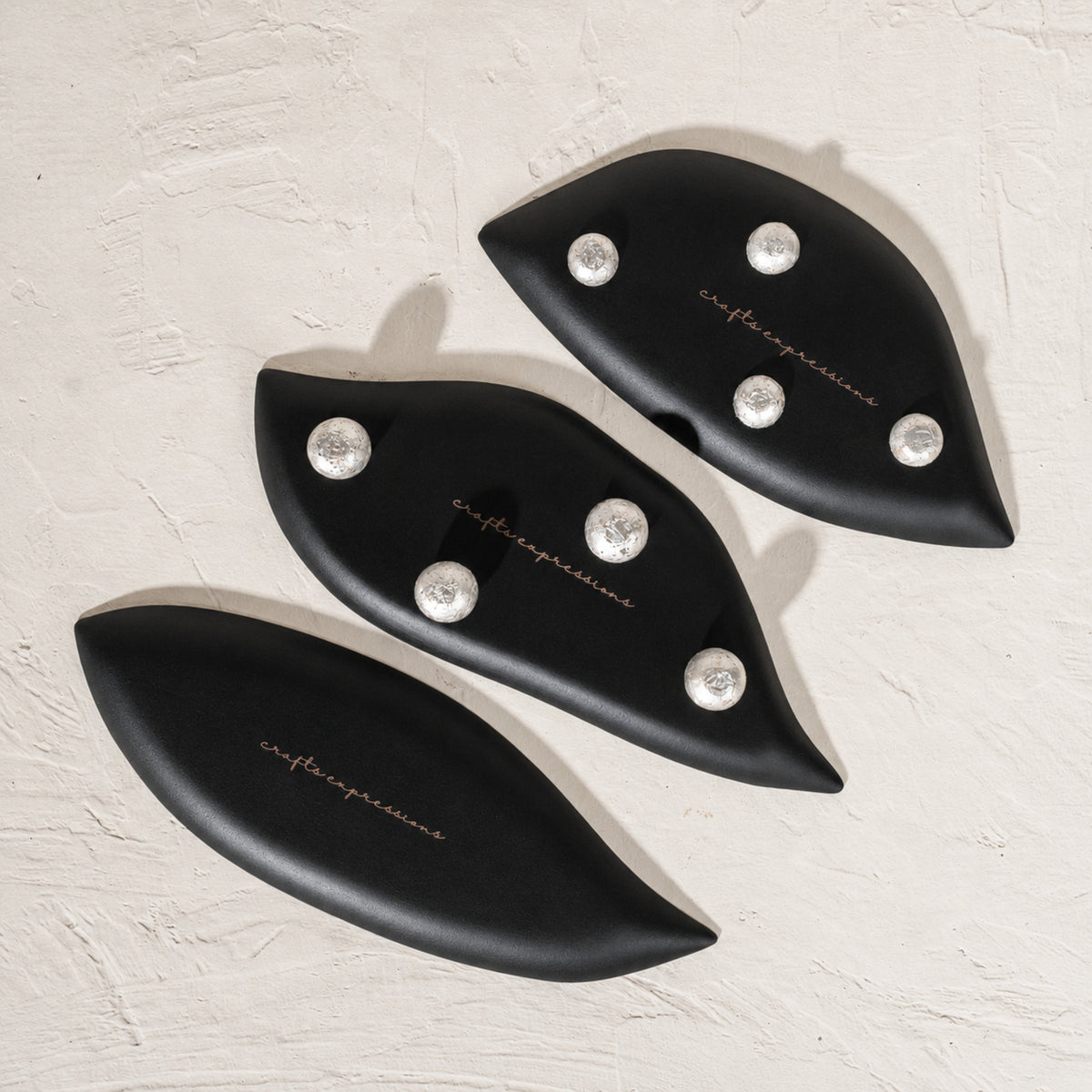 Set of three black wooden leaf-shaped serving platters with carved vein details