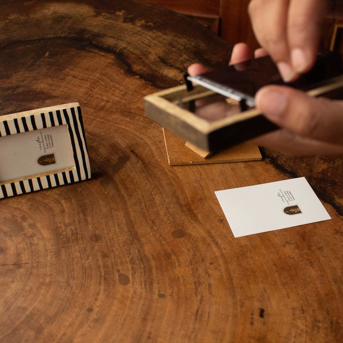 Hands placing an instant photo into a black-and-white striped wooden frame