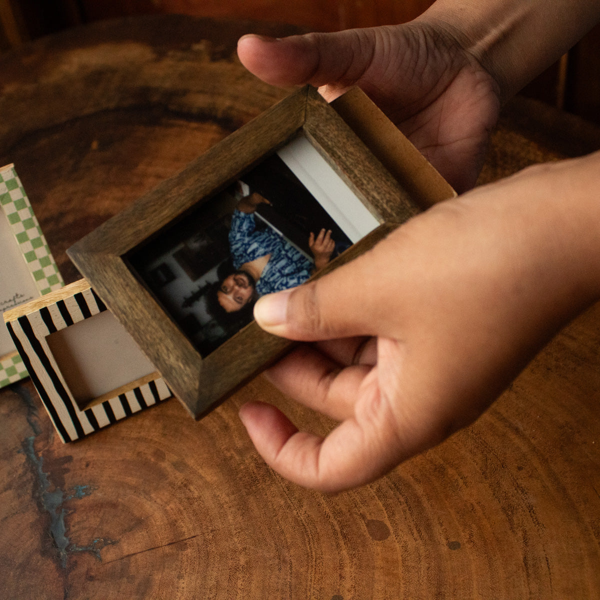 Hands inserting an instant photo into a natural wooden Polaroid photo frame