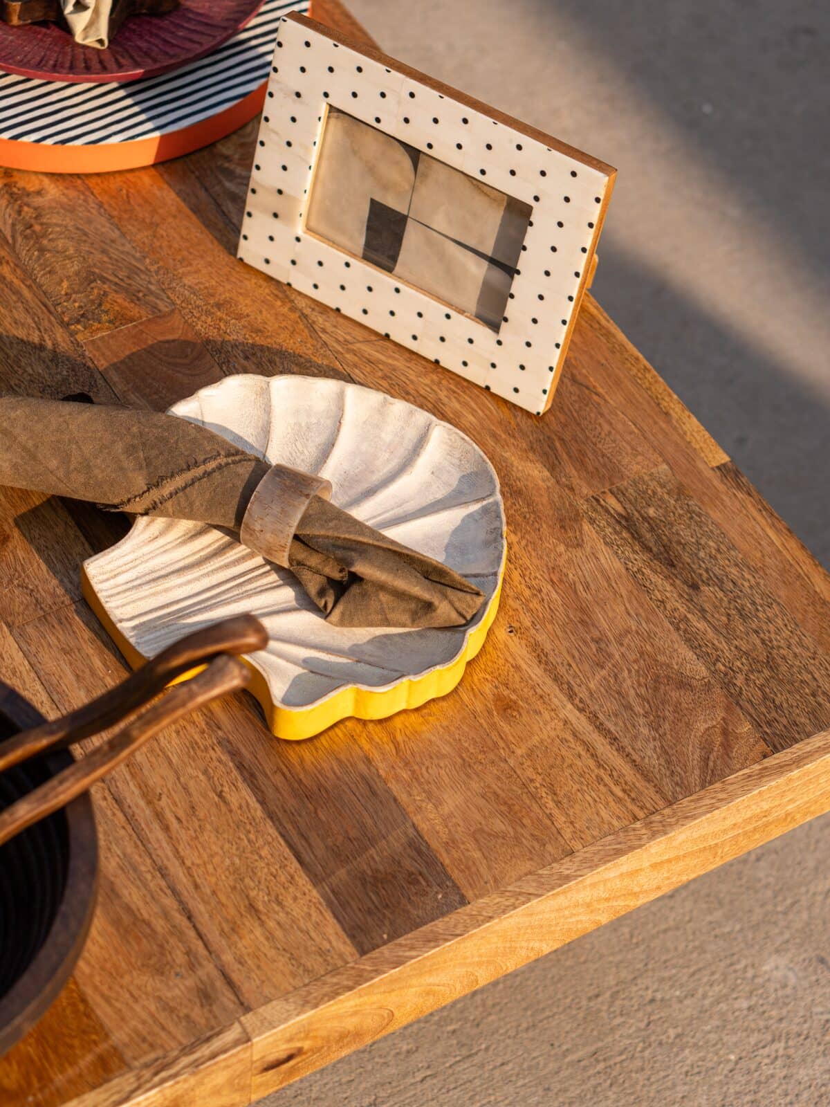 A scalloped ceramic dish with a yellow rim holding a brown napkin, styled on a wooden table next to a white polka-dot picture frame.