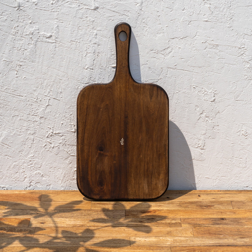 Glide natural wood chopping board standing upright against a textured wall