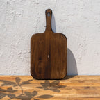 Glide natural wood chopping board standing upright against a textured wall