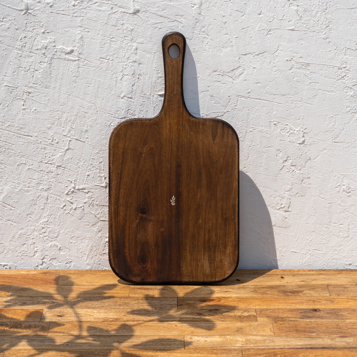 Glide natural wood chopping board standing upright against a textured wall