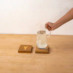 Hand placing a bottle on a square Marine wooden trivet