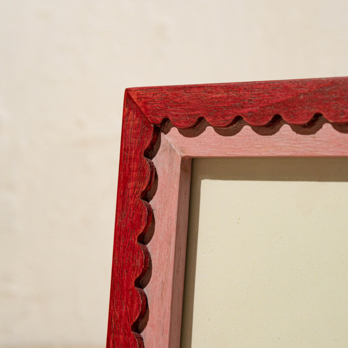 Close-up of the red and pink scalloped edge of the wavy wooden photo frame