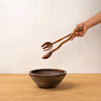 Hand holding a Wavy wooden salad server above a bowl