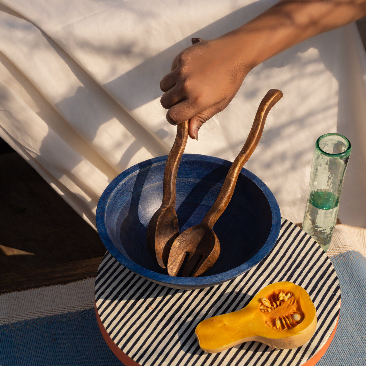 Hand using Wavy wooden salad servers in a serving bowl